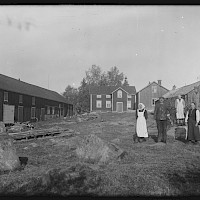 The cottage of Anders Snygg and adherent outbuildings. The people living on the farm gathered in the yard. Replot in 1922.   Photographer: Curt Segerstråle.  Archive collection: The Society of Swedish Literature in Finland (SLS), sls.finna.fi SLS 388_76